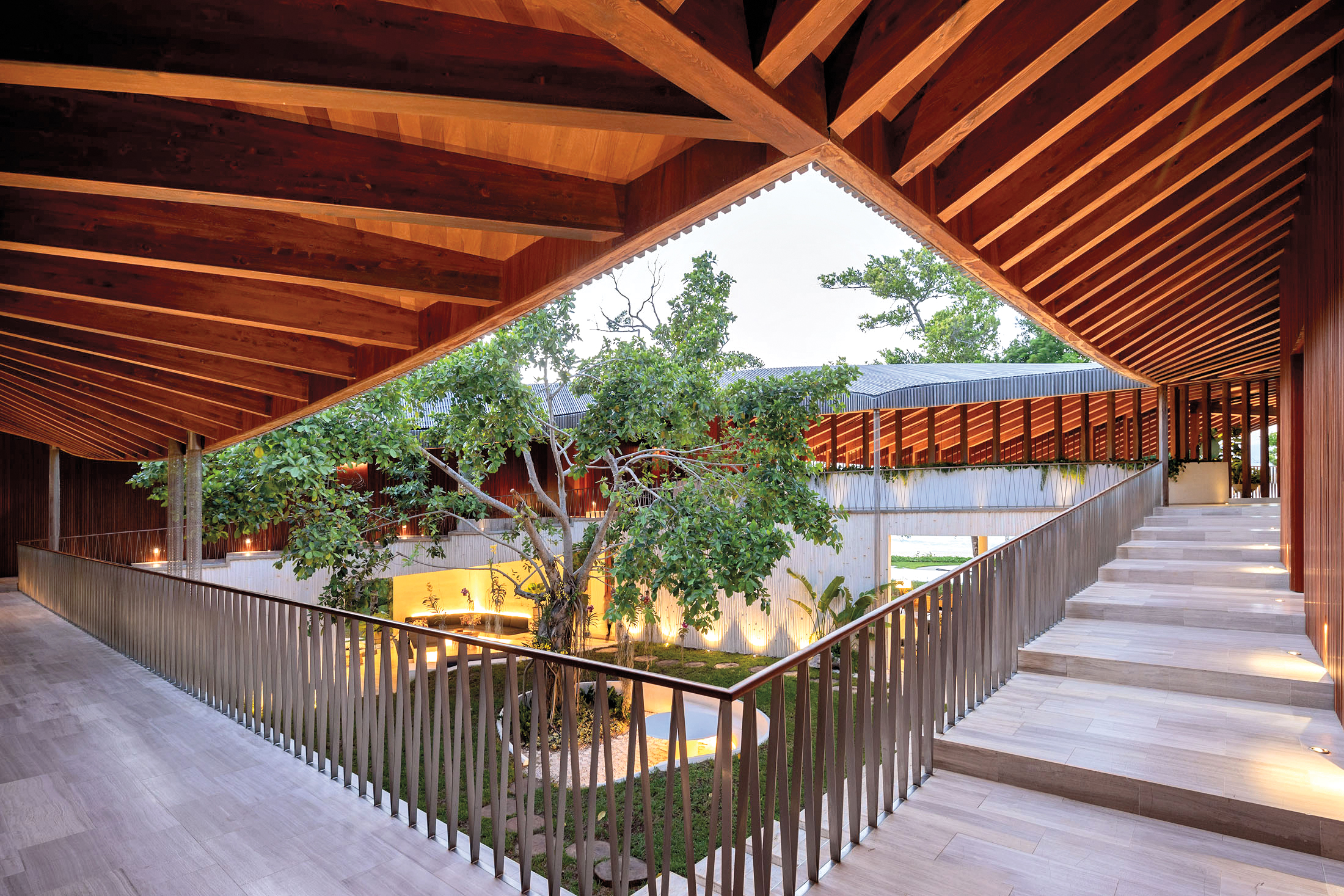 Angular view of a timber roof and outdoor wraparound porch, with a central courtyard that features a tall, tropical tree.