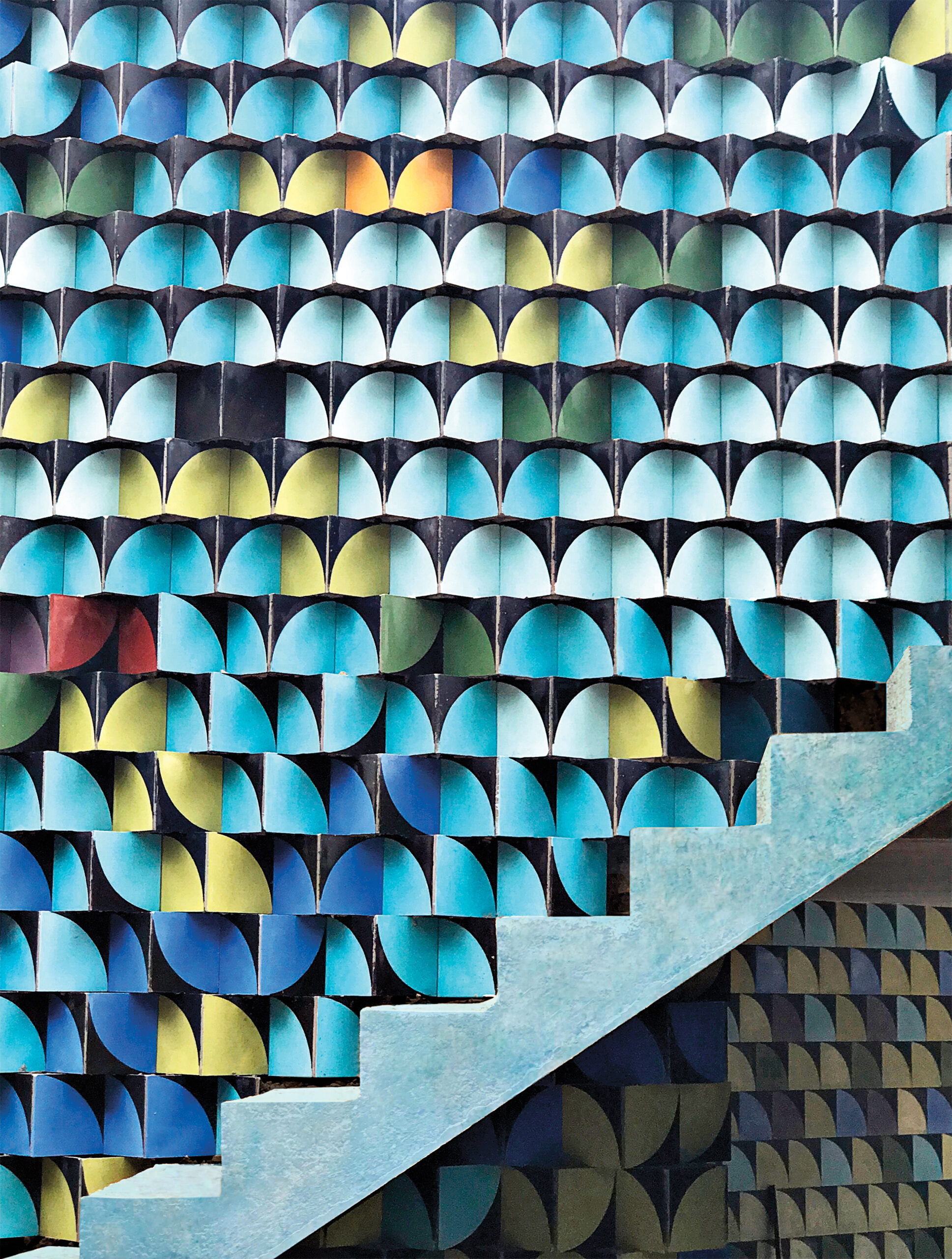 Geometric tile wall with protruding pattern next to staircase in shades of light blue and rainbow.