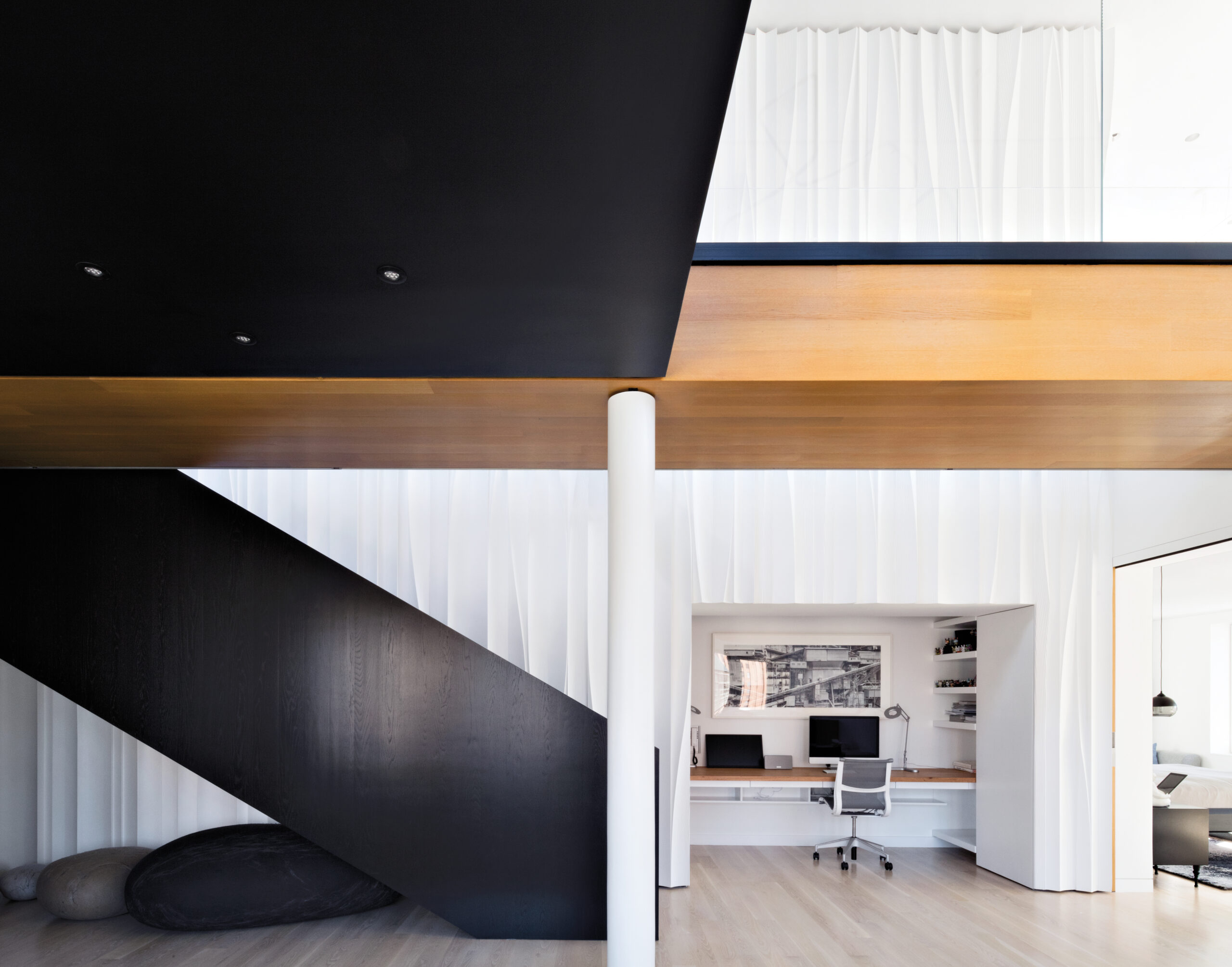 Modern residential interior with large black staircase, white walls, supporting columns and wood.